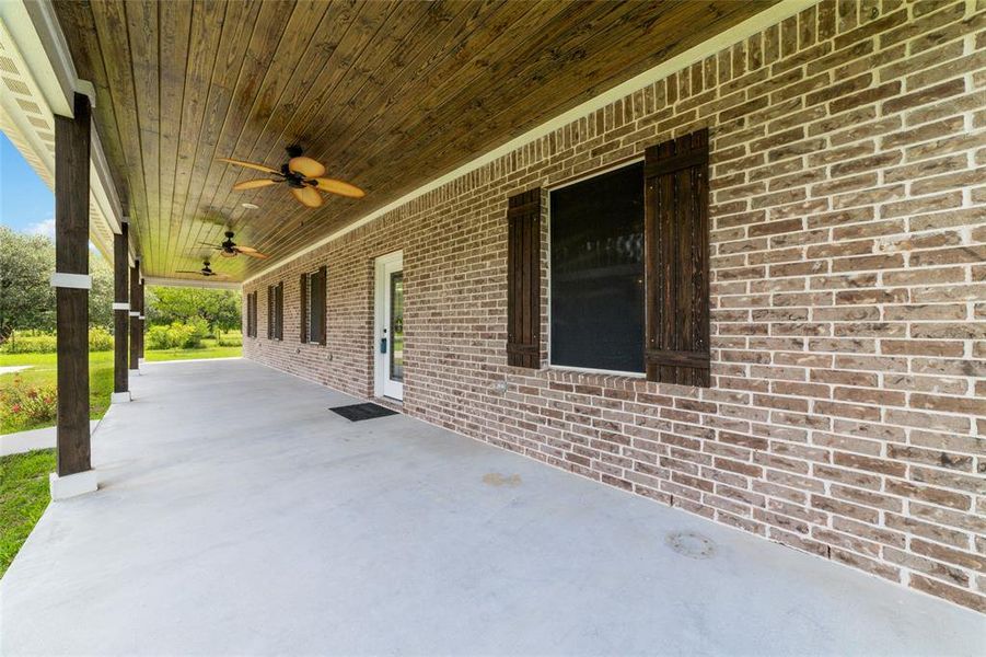 Elegant wooden beams support the covered porch, complemented by a beadboard ceiling and ceiling fans for ultimate comfort. The brick exterior adds a touch of charm, while large windows fitted with solar screens enhance both aesthetics and functionality.