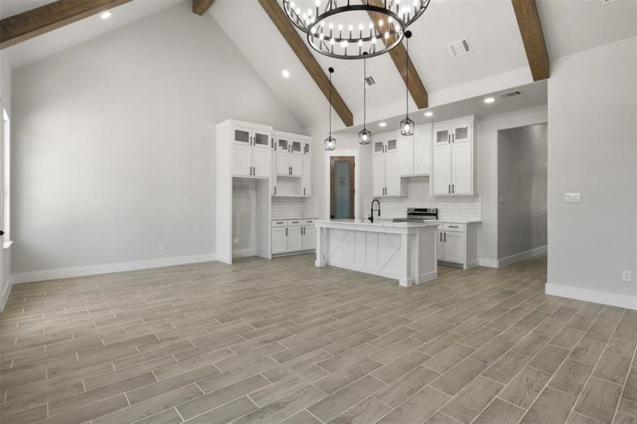 Kitchen featuring an island with sink, light wood-type flooring, backsplash, and white cabinetry