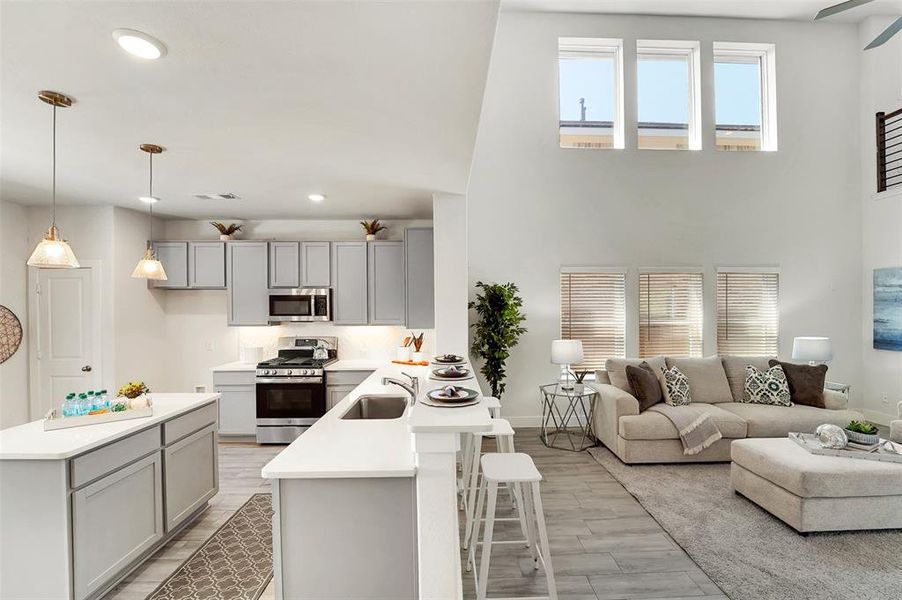 Kitchen featuring light hardwood / wood-style floors, pendant lighting, kitchen peninsula, appliances with stainless steel finishes, and a kitchen breakfast bar