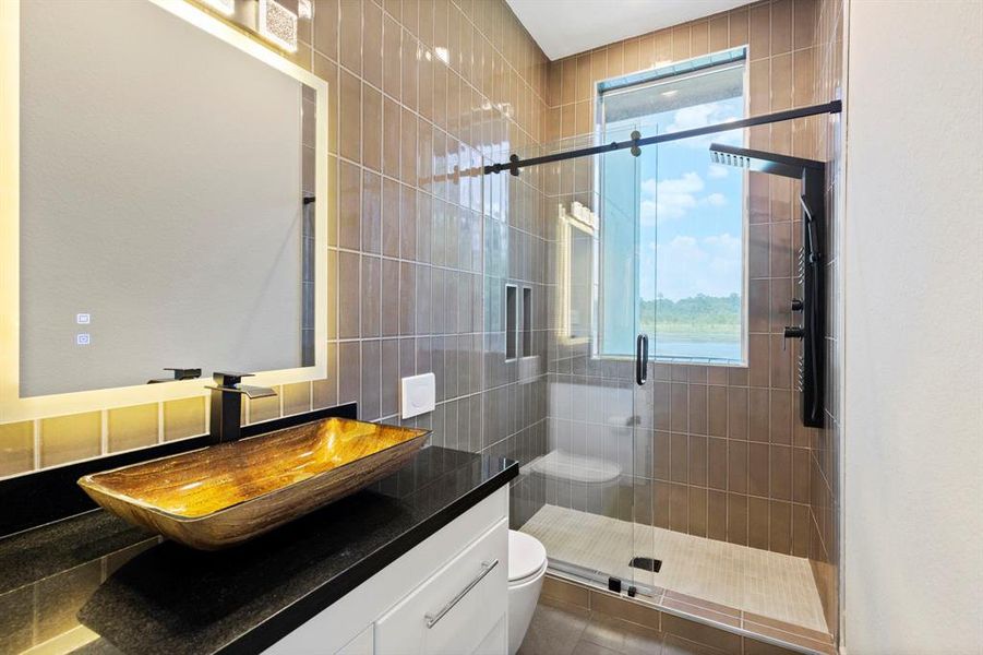 A guest bath that is sure please features a beautiful vessel sink and oversized walk-in shower.