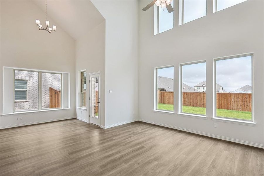 Unfurnished living room with high vaulted ceiling, ceiling fan with notable chandelier, and light hardwood / wood-style flooring