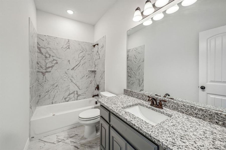 Full bathroom with tiled shower / bath combo, tile patterned floors, toilet, and vanity