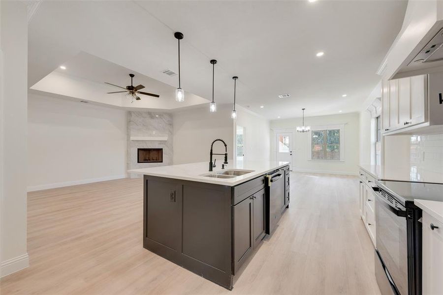 Kitchen with an island with sink, a premium fireplace, sink, white cabinetry, and appliances with stainless steel finishes