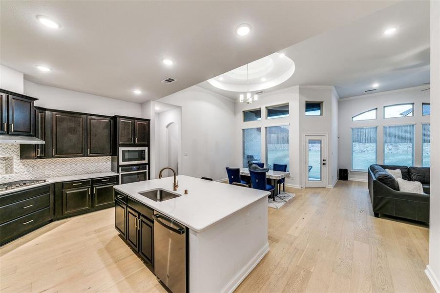 Kitchen featuring tasteful backsplash, appliances with stainless steel finishes, a kitchen island with sink, light wood-type flooring, and sink