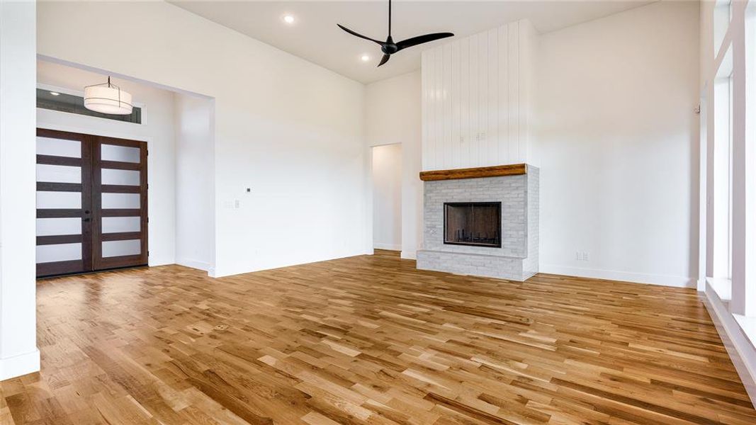 Unfurnished living room featuring high vaulted ceiling, ceiling fan, light hardwood / wood-style floors, and a brick fireplace