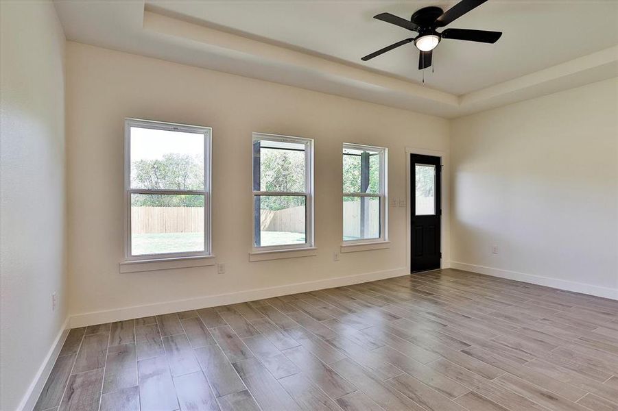 Spare room featuring a tray ceiling, ceiling fan, and light hardwood / wood-style floors