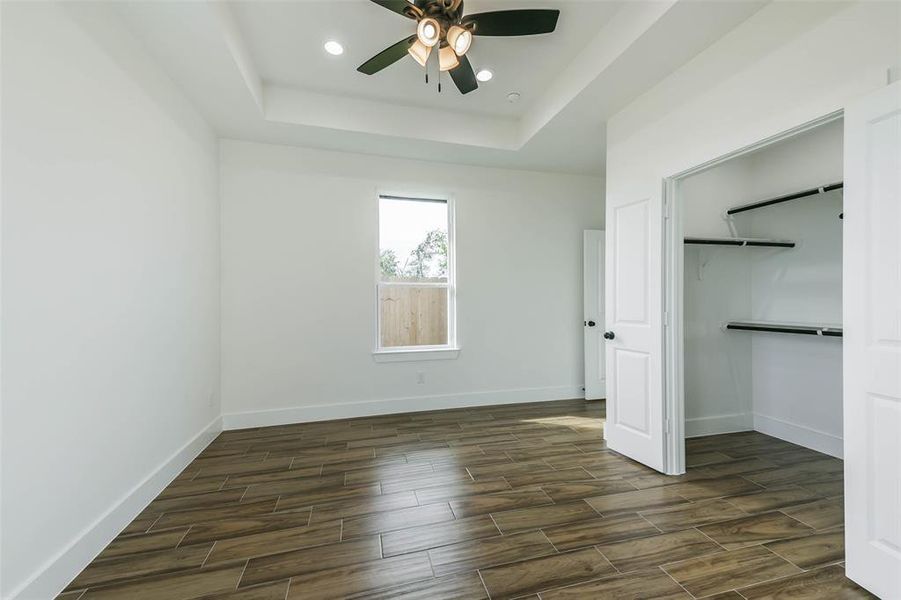 This is a bright, empty room featuring wood-look tile flooring, a ceiling fan with lighting, a large window for natural light, and a built-in closet with shelving for storage.