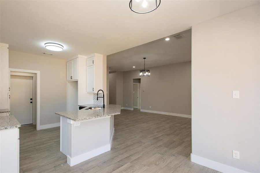 Kitchen featuring light wood-type flooring, white cabinetry, light stone countertops, and pendant lighting