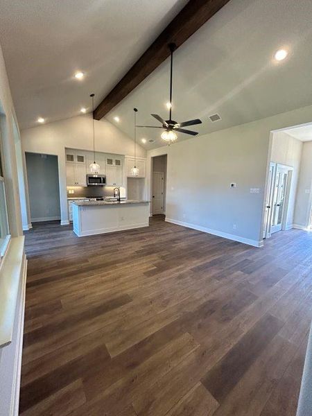 Unfurnished living room featuring lofted ceiling with beams, ceiling fan, dark wood-type flooring, and sink