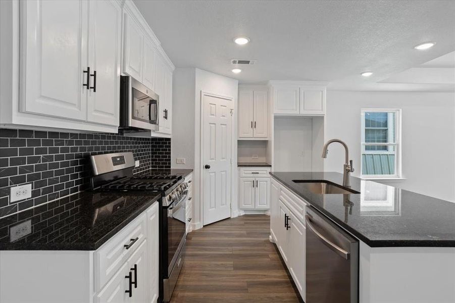 Kitchen with white cabinetry, dark wood-type flooring, appliances with stainless steel finishes, decorative backsplash, and sink