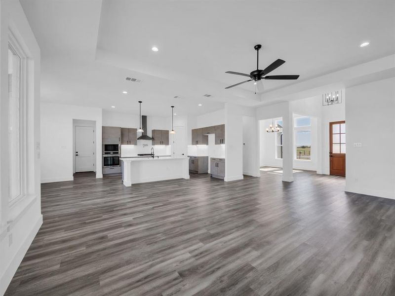 Unfurnished living room with sink, a tray ceiling, ceiling fan with notable chandelier, and dark hardwood / wood-style flooring