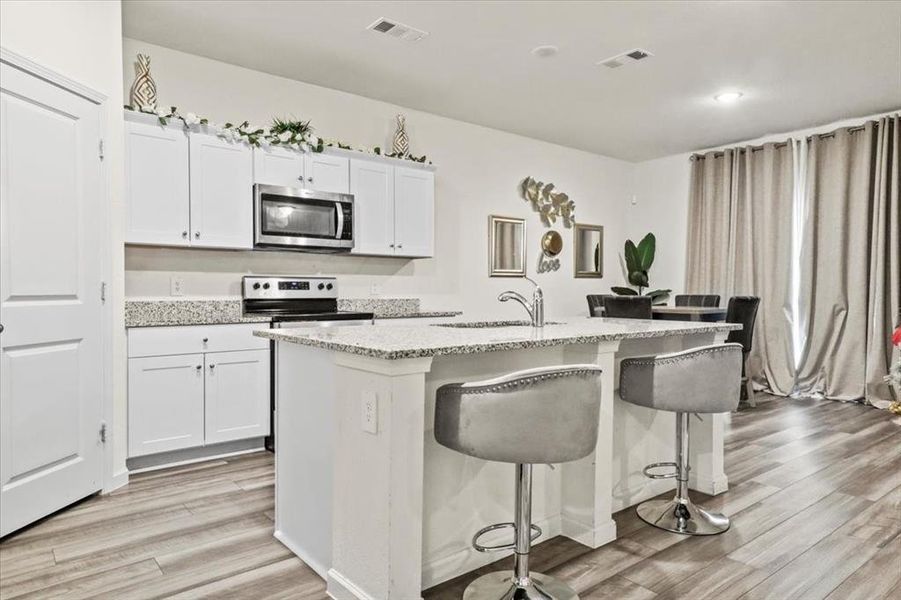 Kitchen with a kitchen bar, a kitchen island with sink, sink, light hardwood / wood-style floors, and white cabinetry