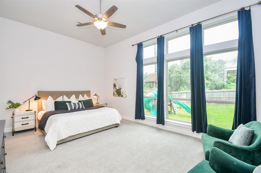 Well-lit primary bedroom featuring neutral walls, newly carpeted flooring, a ceiling fan, and large windows with a view of greenery outside. Also, includes a cozy sitting area for relaxation.