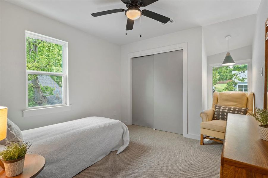 Carpeted bedroom with multiple windows, ceiling fan, closet and nook for desk or reading chair.