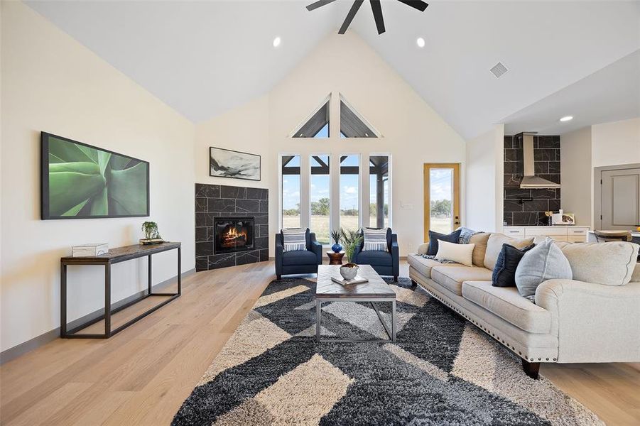 Living room featuring light hardwood / wood-style floors, high vaulted ceiling, a tile fireplace, and ceiling fan