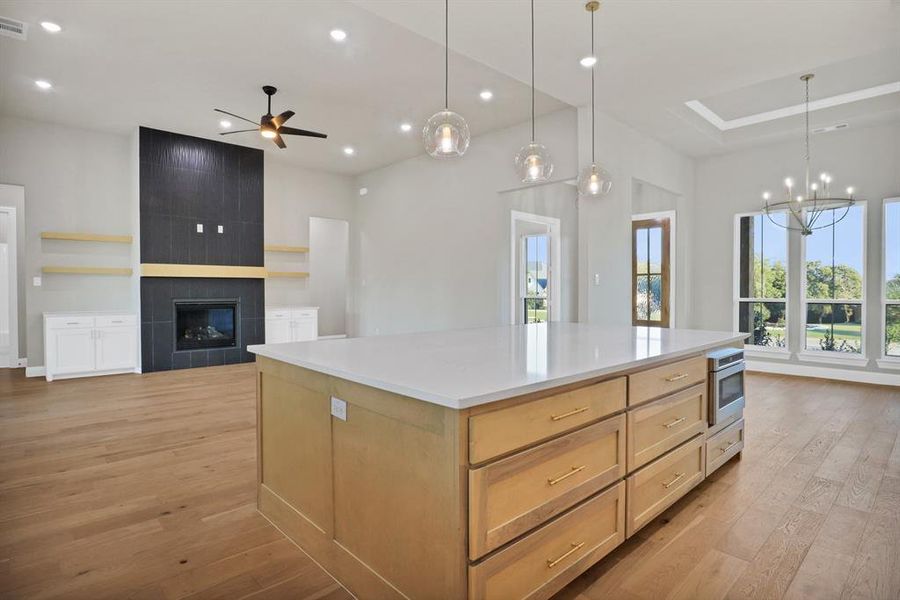 Kitchen featuring light brown cabinets, a large island, light hardwood / wood-style flooring, oven, and a fireplace