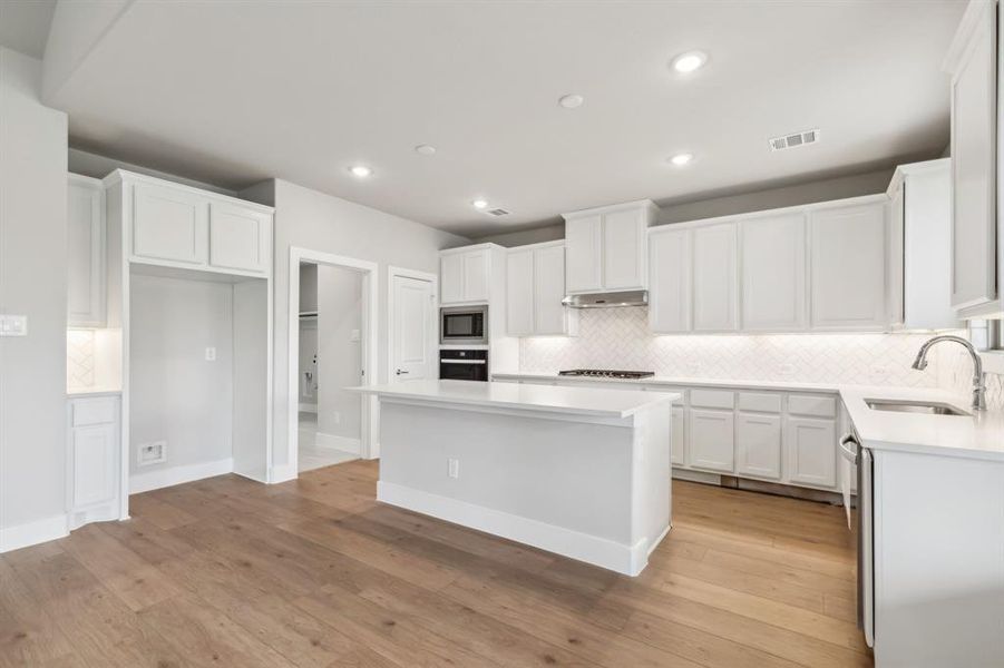 Kitchen featuring light hardwood / wood-style floors, a center island, sink, white cabinetry, and stainless steel appliances