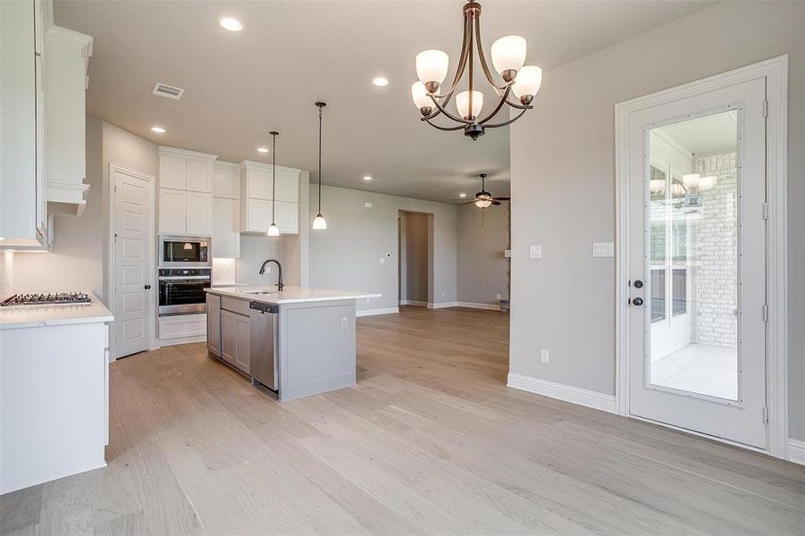 Kitchen featuring ceiling fan with notable chandelier, pendant lighting, stainless steel appliances, a center island with sink, and sink