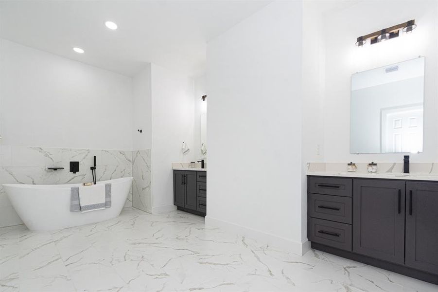 The primary bathroom has two separate self-closing custom wood cabinet/vanities with quartz countertops, elegant mirrors, modern lighting and plumbing fixtures.  The separate soaker tub exudes rest and relaxation.