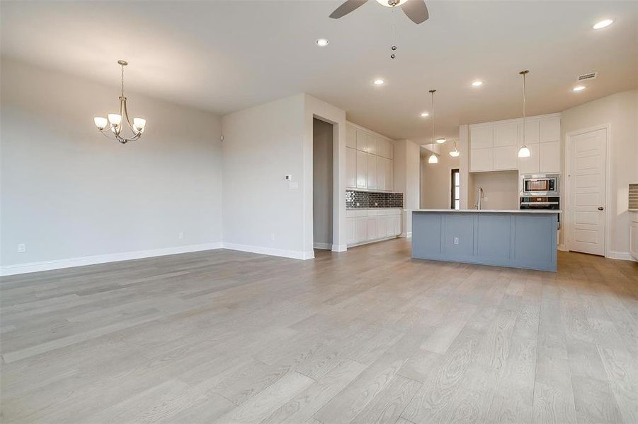 Unfurnished living room with sink, ceiling fan with notable chandelier, and light wood-type flooring