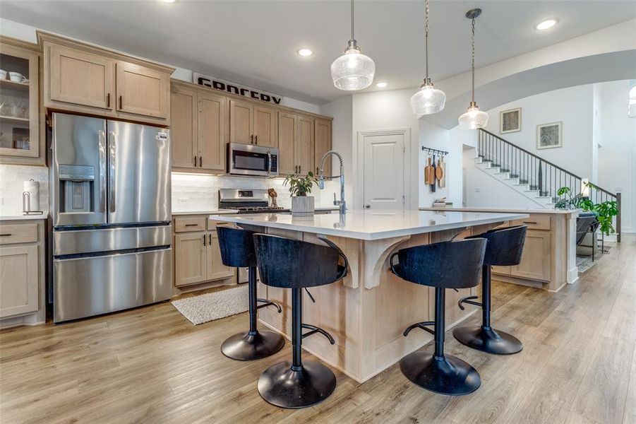 Kitchen featuring light hardwood / wood-style flooring, a quartz island with sink, decorative light fixtures, backsplash, and appliances with stainless steel finishes