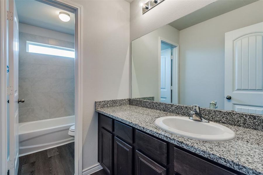 Full bathroom with wood-type flooring, tiled shower / bath, vanity, and toilet