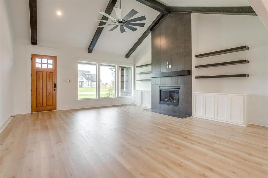 Unfurnished living room with beamed ceiling, a tile fireplace, light hardwood / wood-style flooring, high vaulted ceiling, and ceiling fan