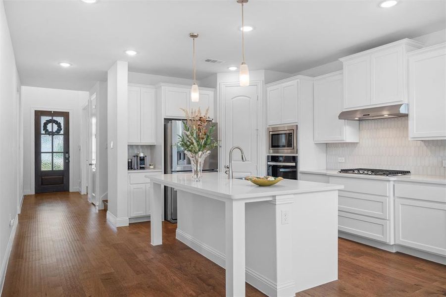 Kitchen with white cabinetry, stainless steel appliances, ventilation hood, and an island with sink