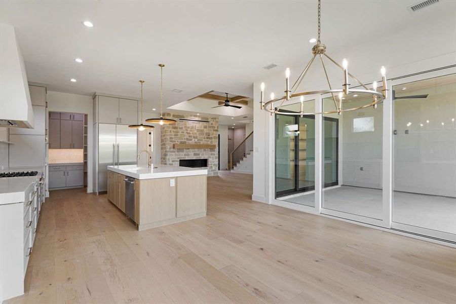 Kitchen featuring a large island, light wood-type flooring, ceiling fan with notable chandelier, decorative light fixtures, and a stone fireplace