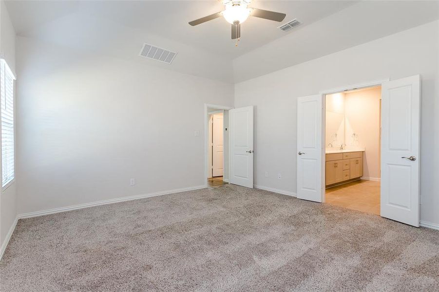 Primary bedroom with light carpet, ceiling fan, and ensuite bath