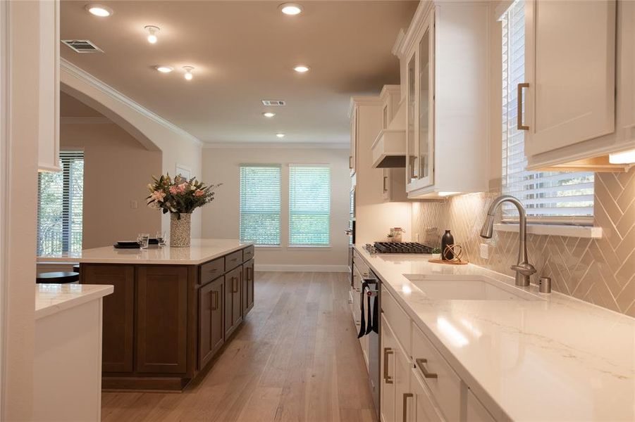 Kitchen with dark brown cabinets, white cabinetry, light hardwood / wood-style floors, crown molding, and sink