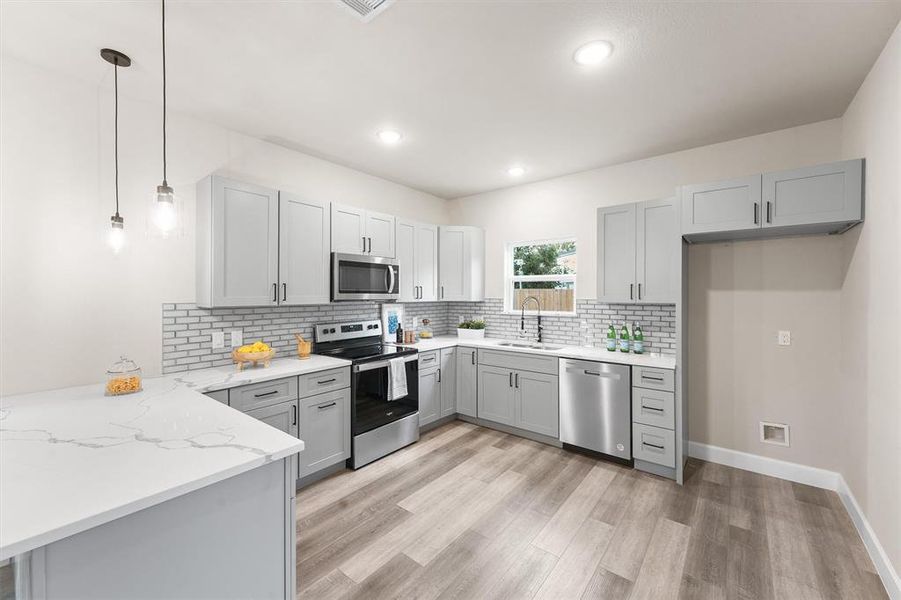 Modern kitchen with stainless steel appliances, white marbled countertops, sleek gray cabinetry, and subway tile backsplash. Bright, with recessed lighting and pendant lights.