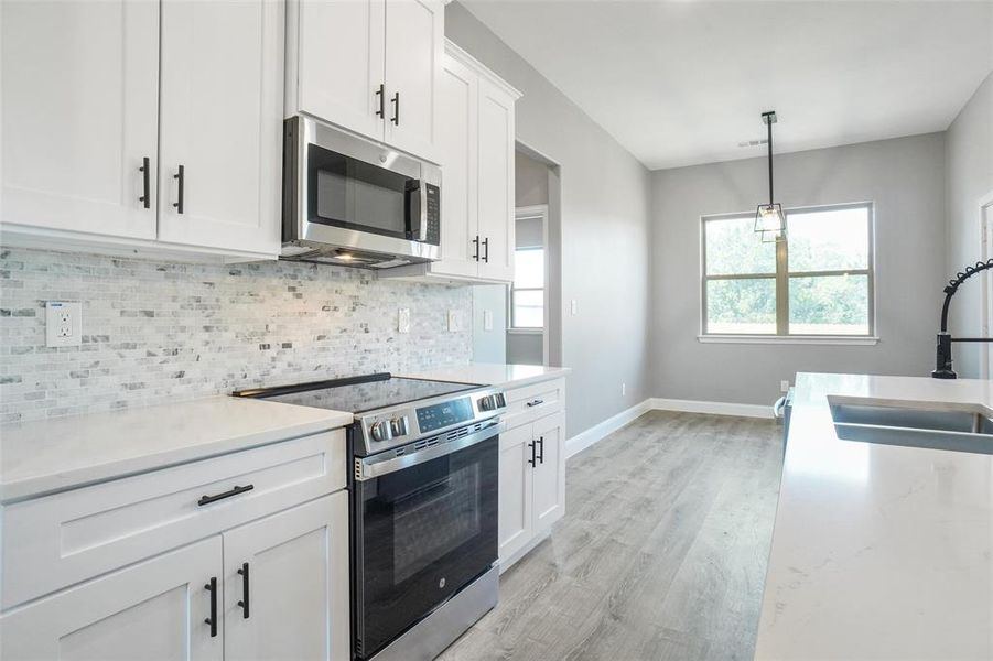 Kitchen featuring stainless steel appliances, white cabinets, sink, decorative backsplash, and light wood-type flooring