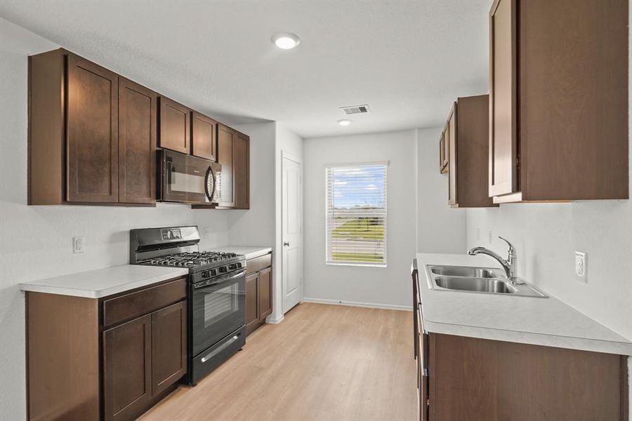 You'll love the details of this kitchen! It features sleek wood cabinets, white countertops, recessed lighting, wood like flooring, and a gas stove!