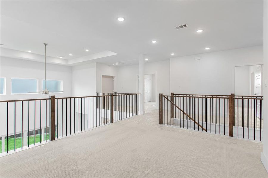 Hallway featuring a raised ceiling, light colored carpet, and a wealth of natural light