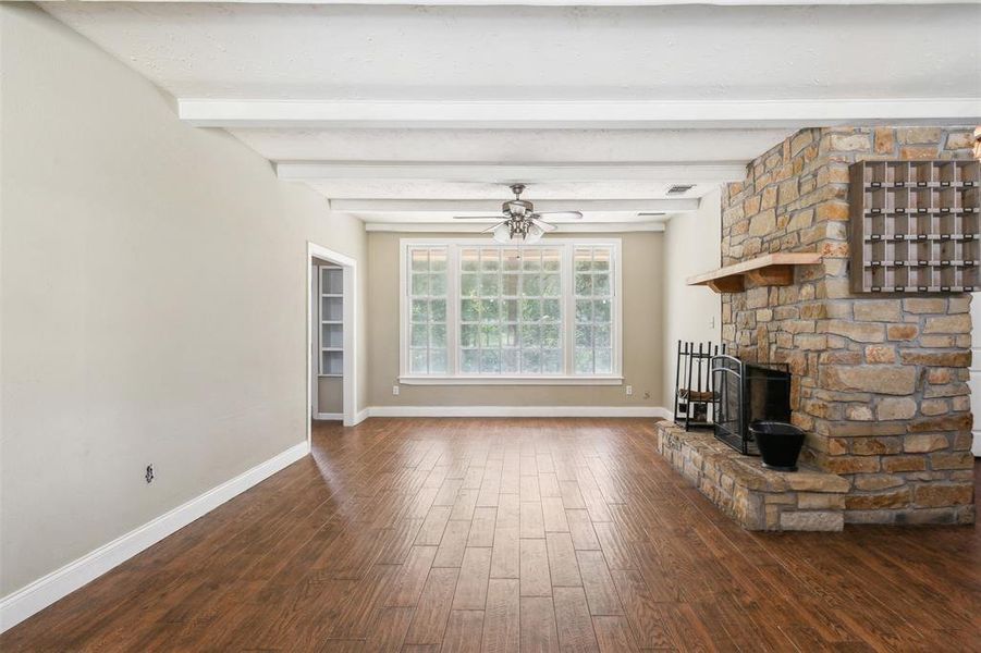 Family room featuring ceiling fan, beamed ceiling, a stone fireplace, and dark wood-type flooring