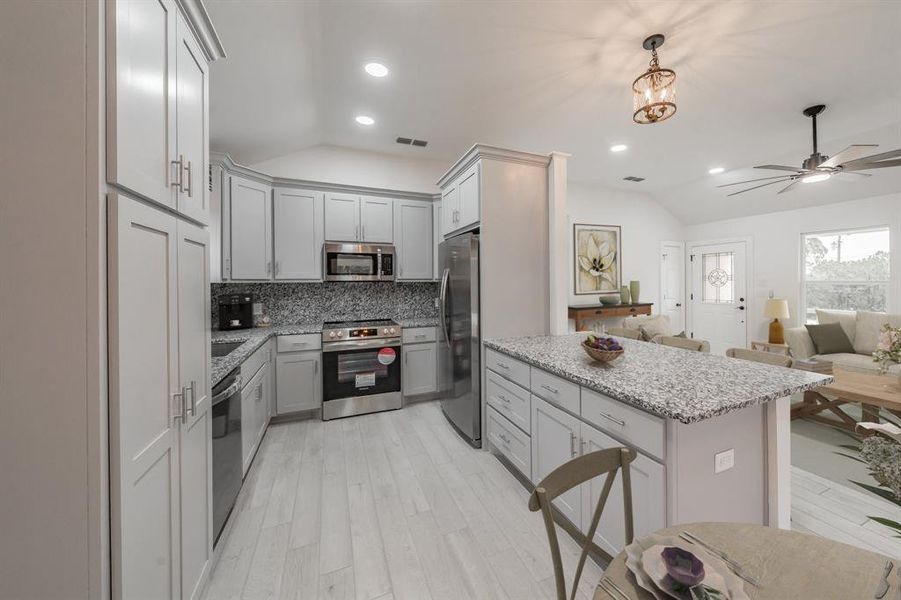 Kitchen featuring stainless steel appliances, hanging light fixtures, lofted ceiling, and gray cabinetry