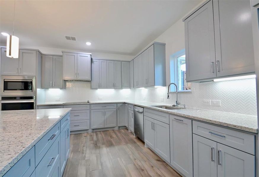 Kitchen featuring appliances with stainless steel finishes, light hardwood / wood-style floors, pendant lighting, gray cabinets, and sink