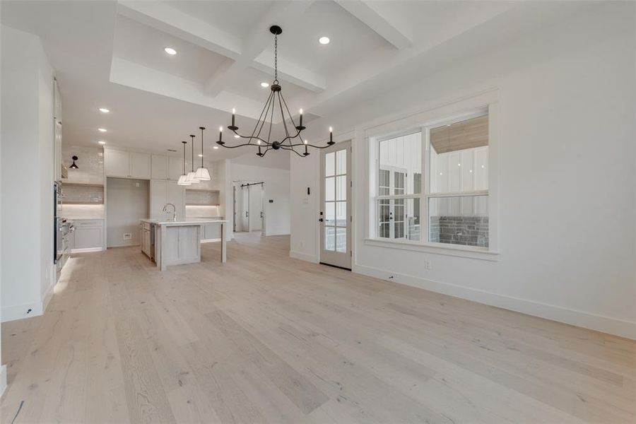 Unfurnished living room with light hardwood / wood-style floors, a notable chandelier, coffered ceiling, and beamed ceiling