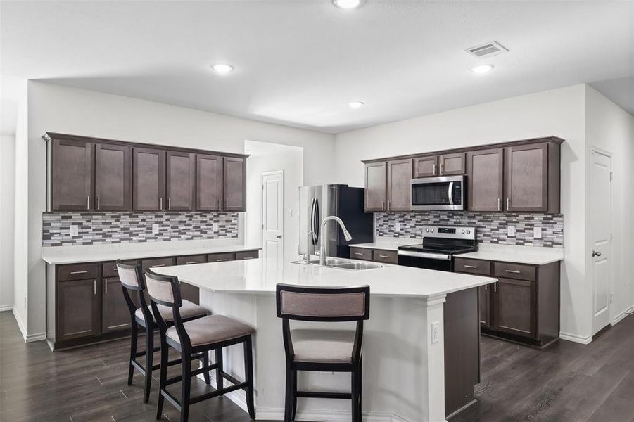 Kitchen featuring dark wood-type flooring, stainless steel appliances, and an island with sink