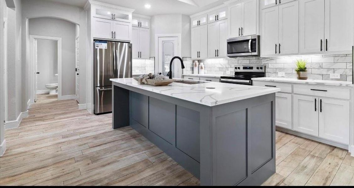 Kitchen with appliances with stainless steel finishes, light stone counters, white cabinets, light hardwood / wood-style flooring, and a kitchen island with sink