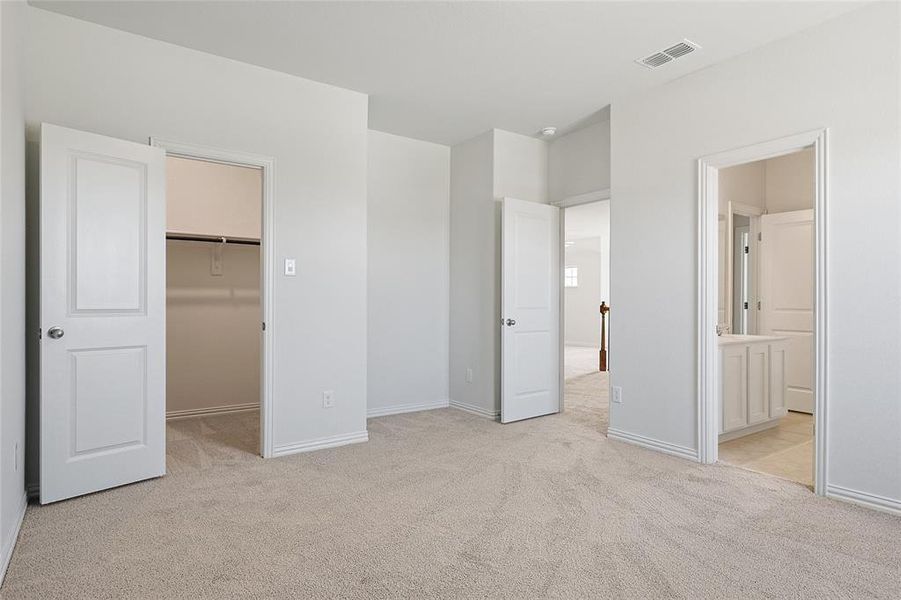 Unfurnished bedroom with light colored carpet, a closet, a walk in closet, and ensuite bathroom