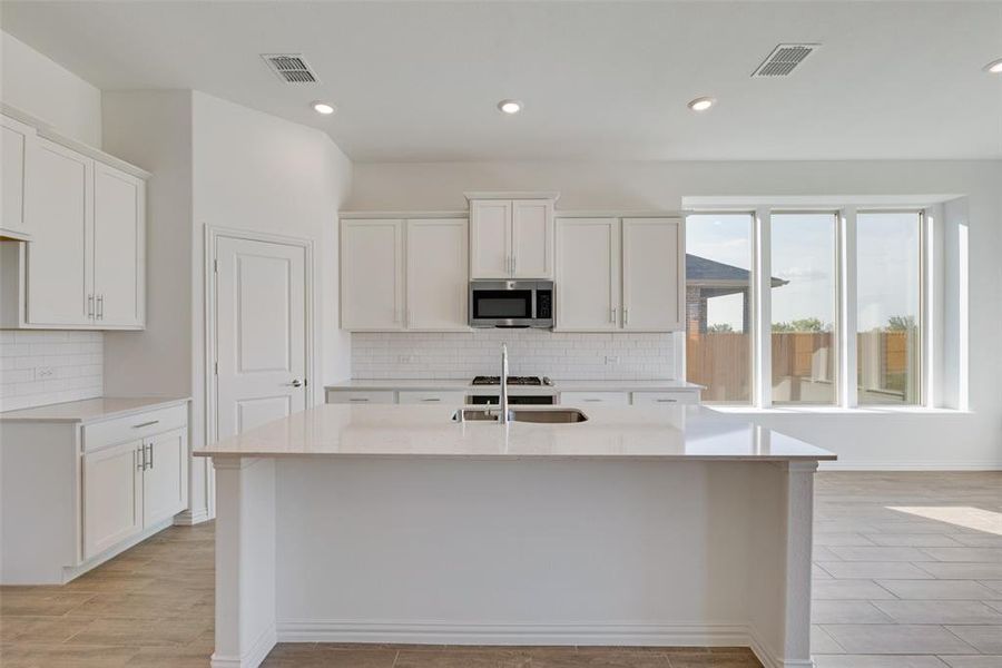 Kitchen with white cabinetry, backsplash, and a kitchen island with sink