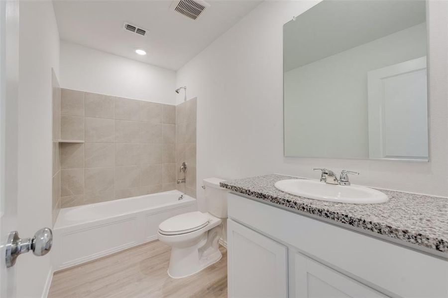 Full bathroom with tiled shower / bath combo, vanity, toilet, and hardwood / wood-style flooring