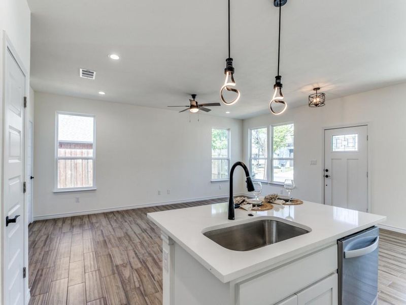 Kitchen featuring light wood-type flooring, white cabinetry, stainless steel dishwasher, pendant lighting, and a center island with sink