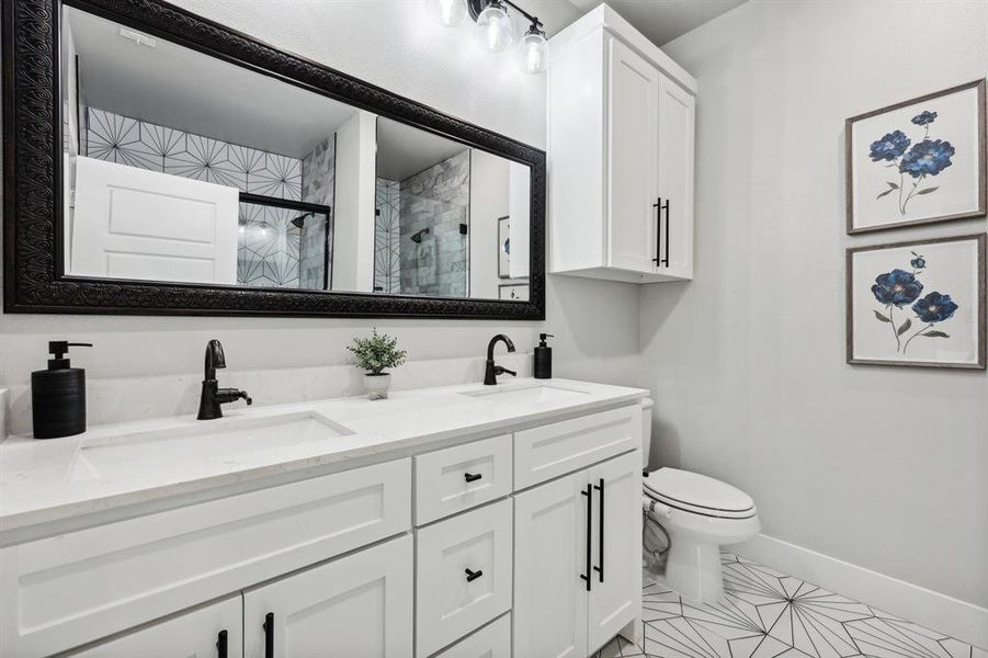 Bathroom with an enclosed shower, toilet, tile patterned floors, and dual bowl vanity