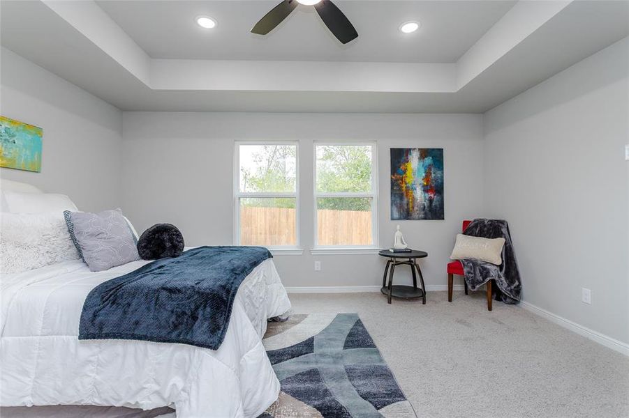 Carpeted bedroom with a raised ceiling and ceiling fan