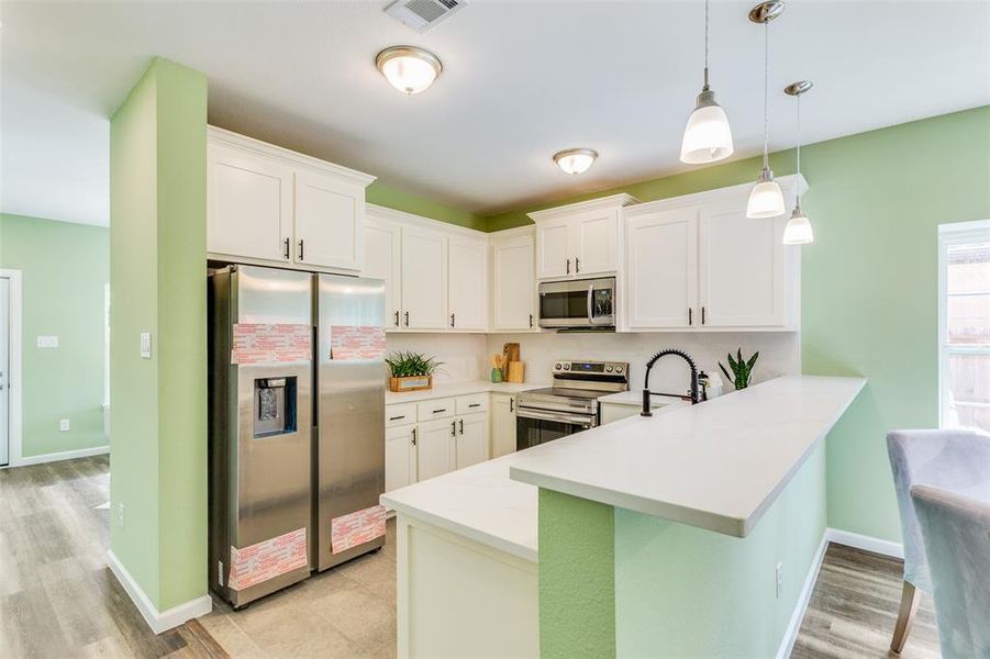 Kitchen with light hardwood / wood-style flooring, kitchen peninsula, white cabinets, stainless steel appliances, and hanging light fixtures