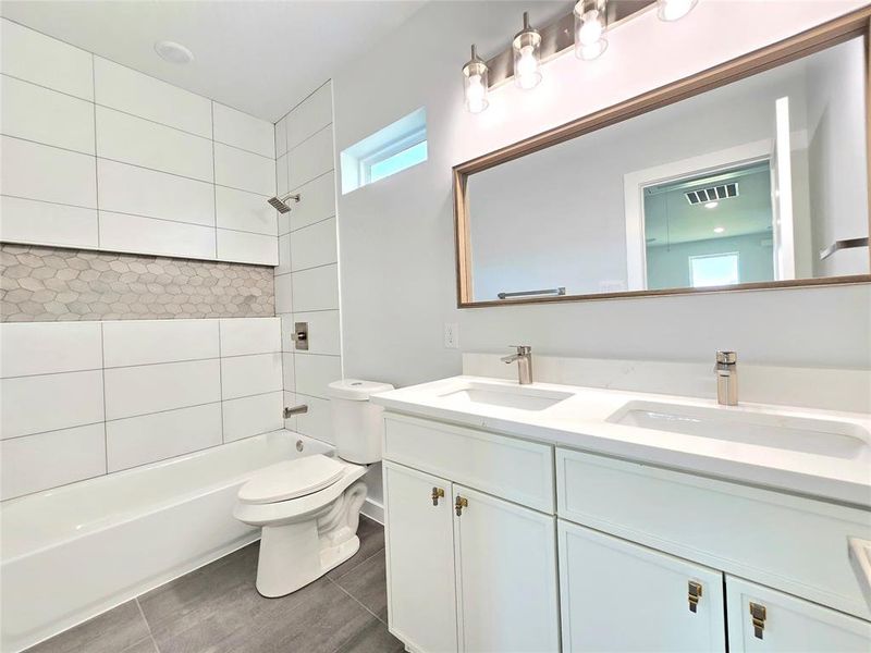 Full bathroom with tiled shower / bath combo, toilet, tile patterned floors, and dual vanity