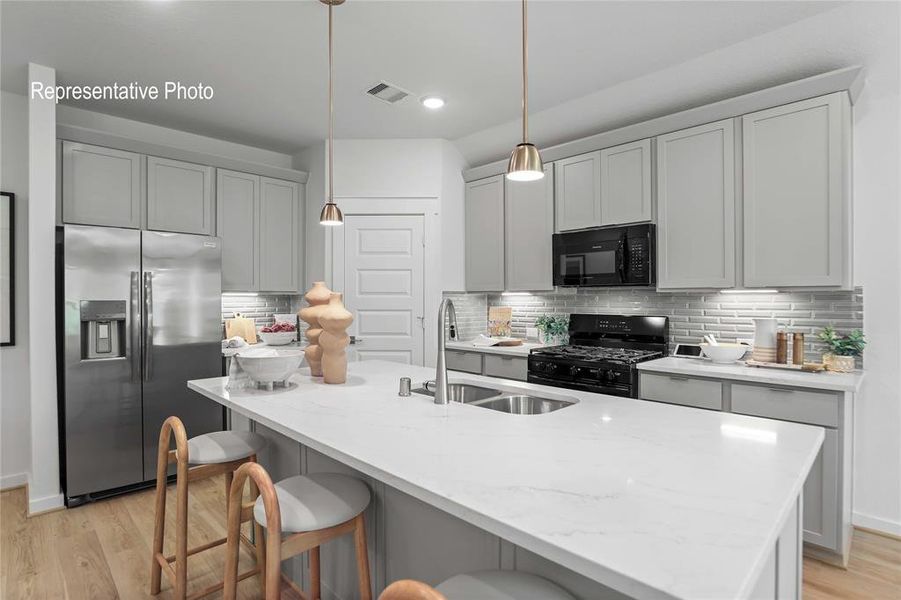 Kitchen with a center island with sink, black appliances, sink, and light wood-type flooring